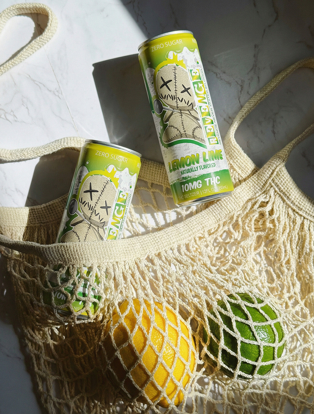 Two cans of lemon lime soda on a textured surface with a mesh bag and fruits.